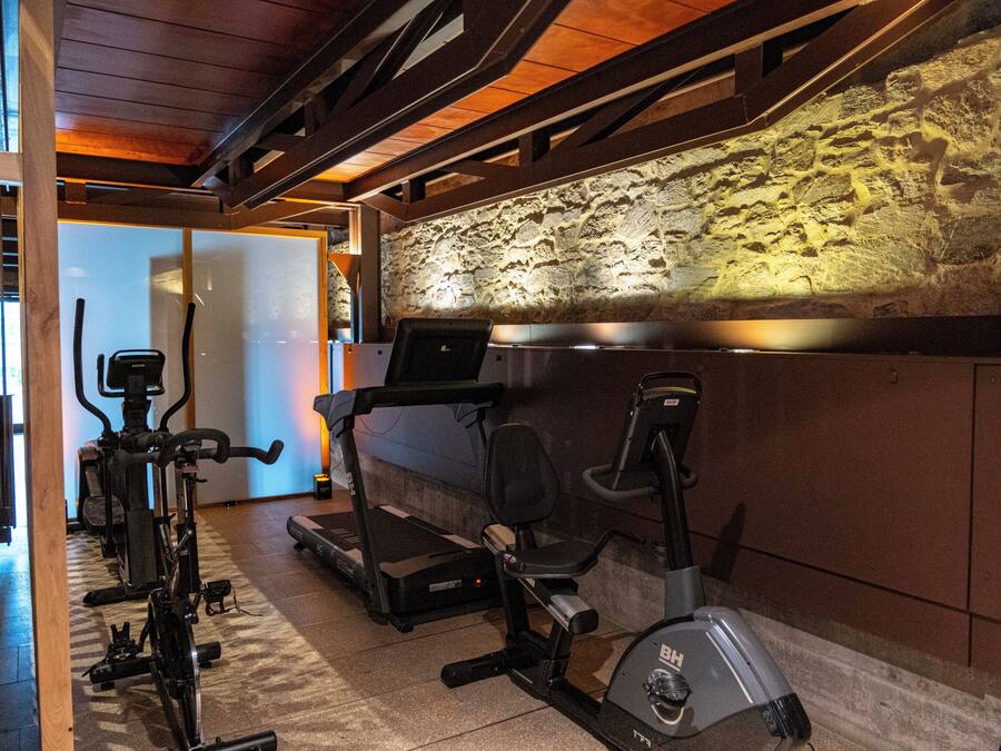 A gym with exercise equipment including treadmills and stationary bikes, a stone wall, and wooden beams on the ceiling.