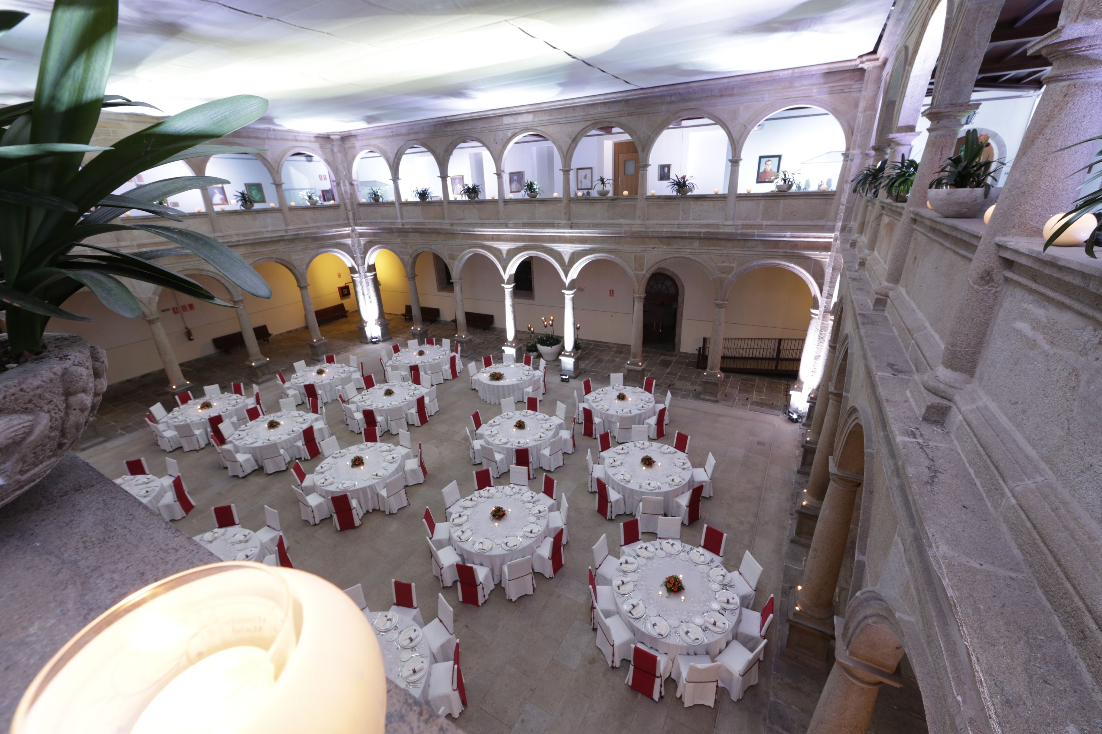 Une vaste cour intérieure agrémentée de nombreuses tables rondes disposées pour les repas, entourée d’arcades et de colonnes.