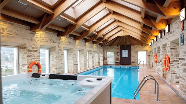 An indoor swimming pool with a hot tub, stone walls, wooden beams, and lifebuoys.