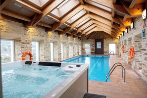 Une piscine intérieure dotée d’un jacuzzi, de murs en pierre, de poutres en bois et de bouées de sauvetage.