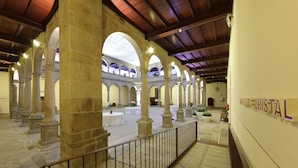 A spacious hall with high stone columns, a tiled floor, and a staircase leading to an upper level.