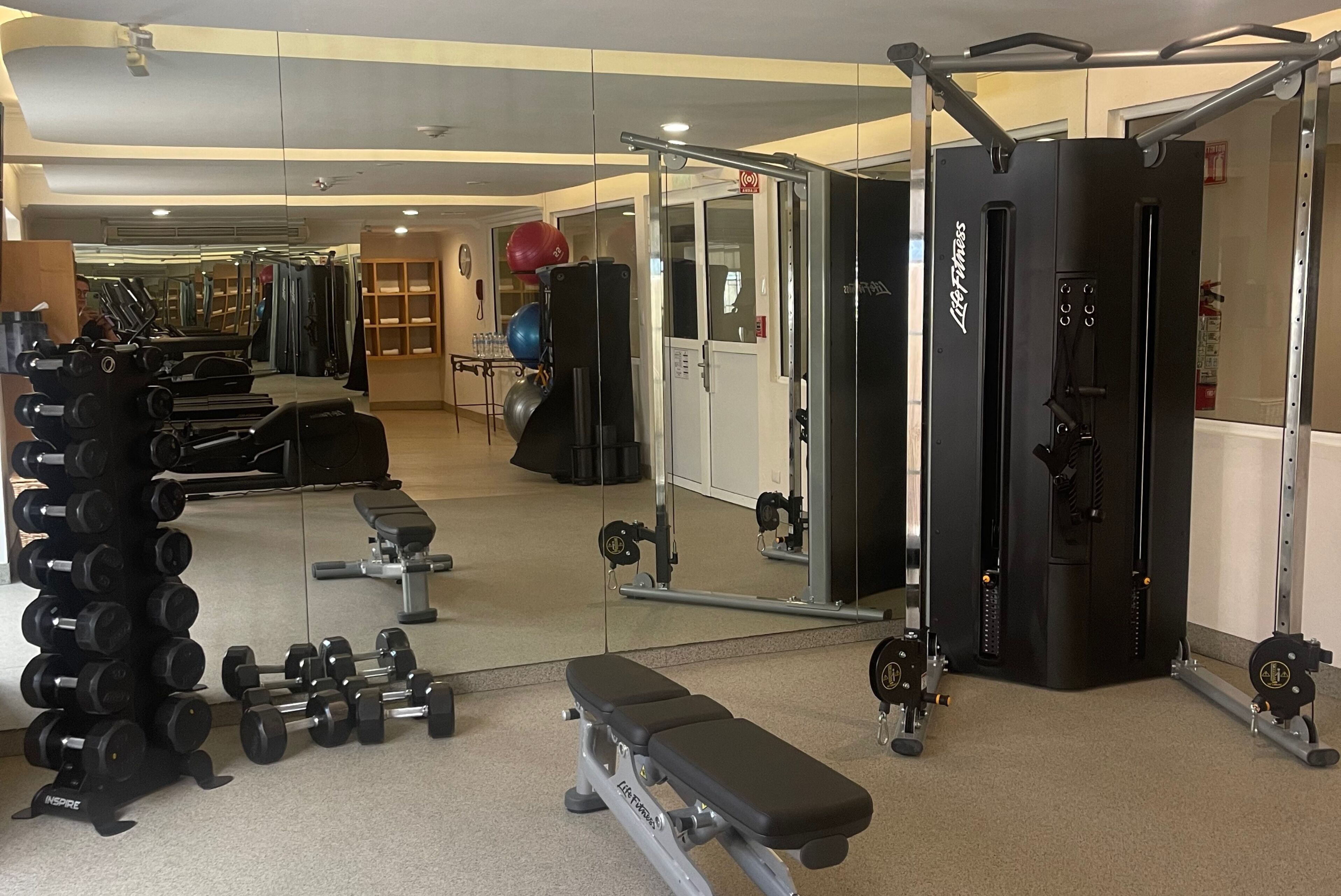 Un gimnasio con varios equipos de ejercicio, incluyendo mancuernas, un banco y una máquina de poleas.