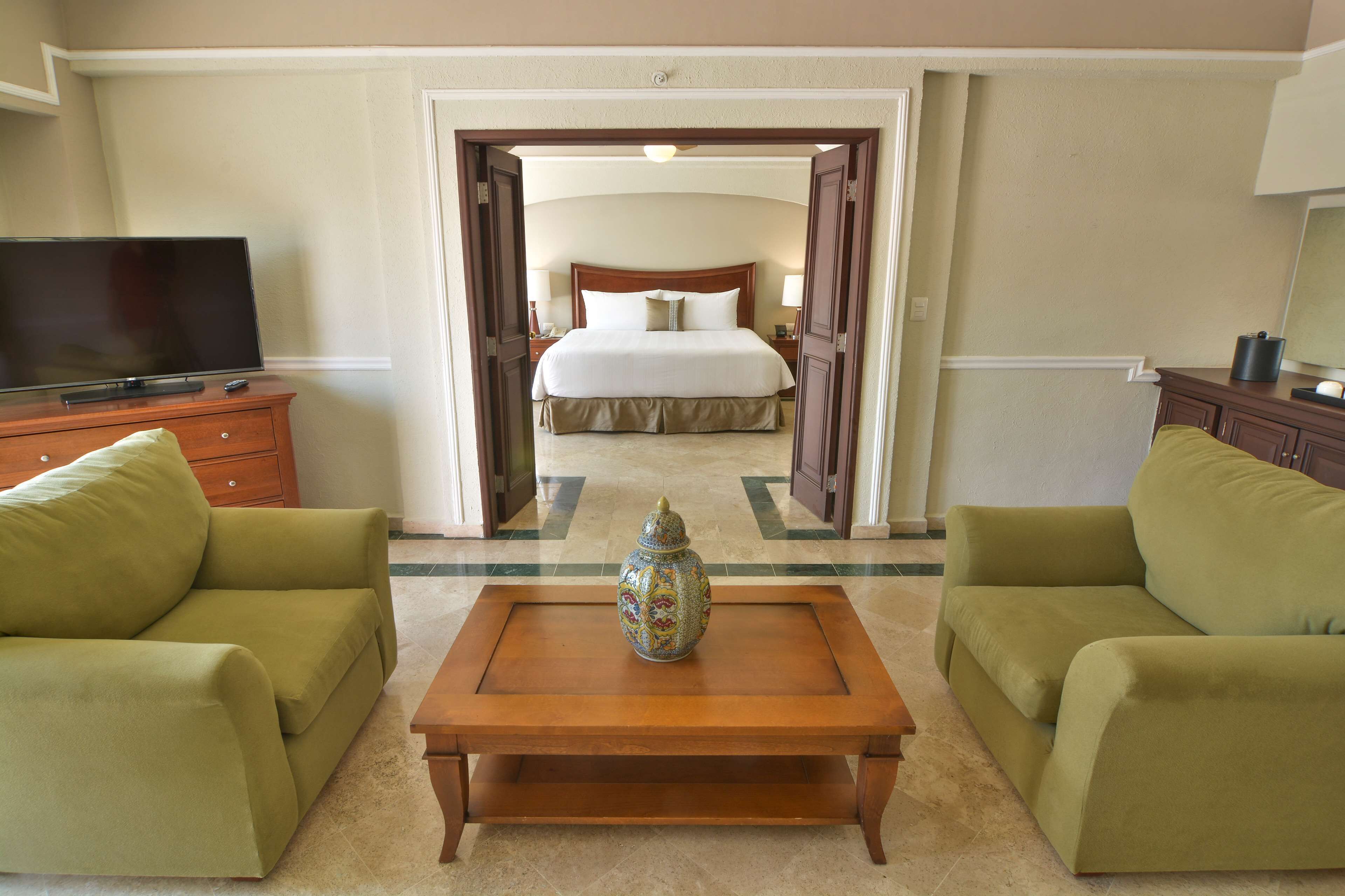 A hotel room with a bed, a television, and two green sofas.