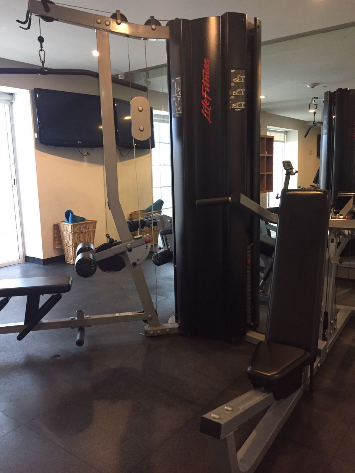 A gym with weightlifting equipment, a bench, and a wall-mounted TV.