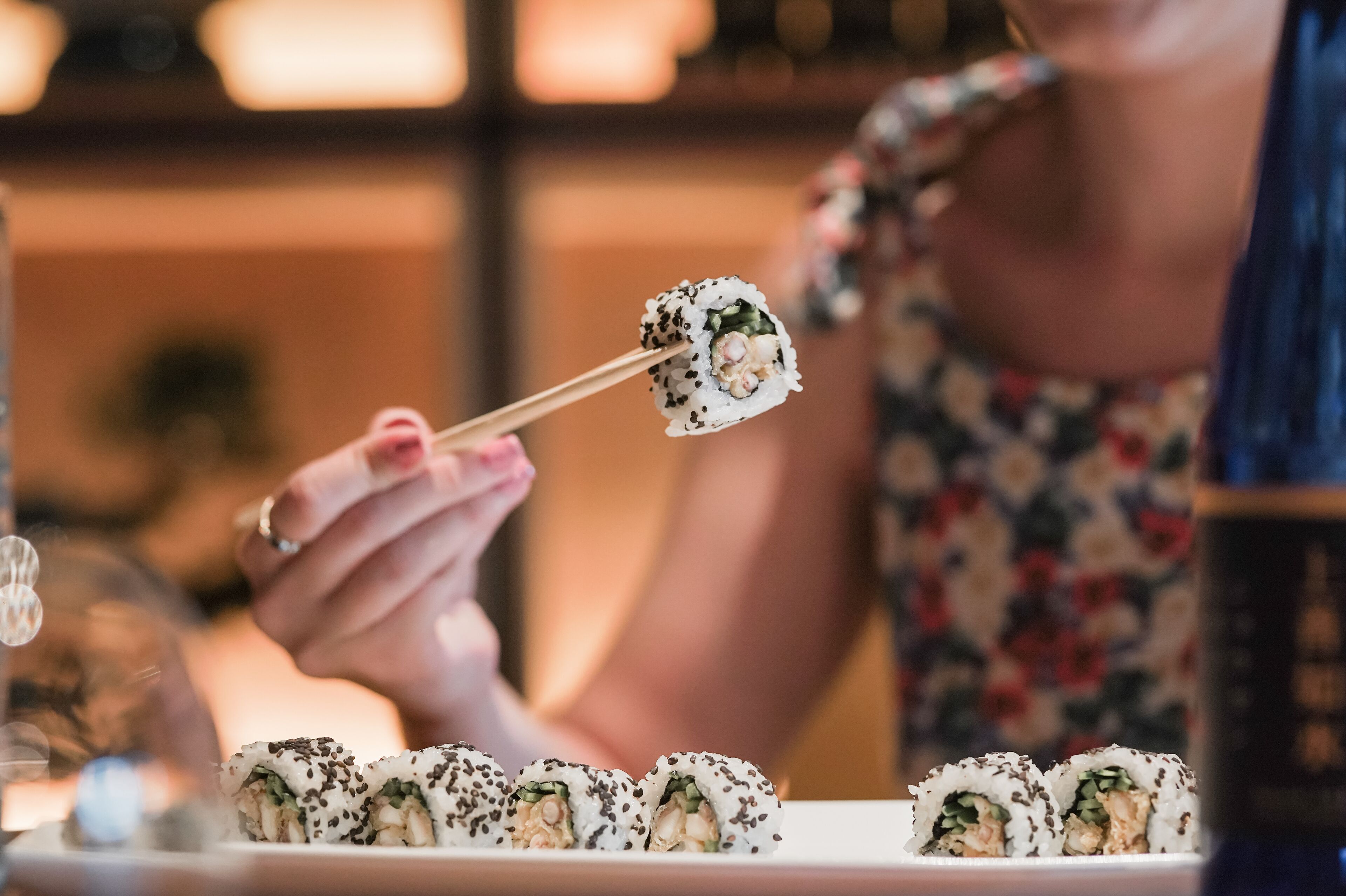Une personne tenant un rouleau de sushis à l’aide de baguettes.