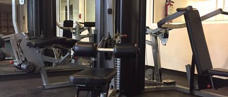 Un gimnasio con diversas máquinas de ejercicio, incluyendo una jaula de sentadillas, una prensa de piernas y un banco de press.