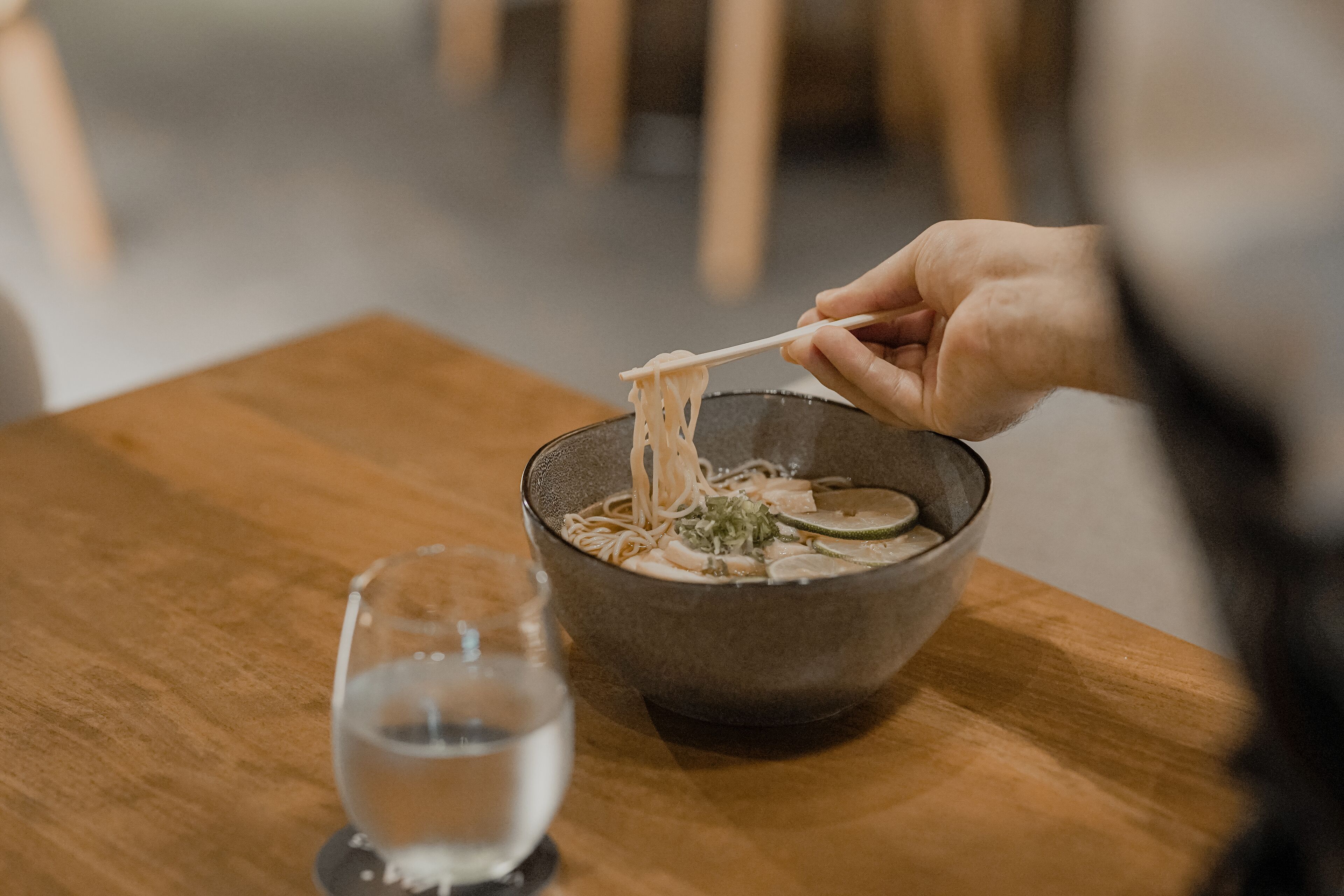 A bowl of ramen noodles with a clear broth, garnished with green onions and mushrooms, on a wooden table.