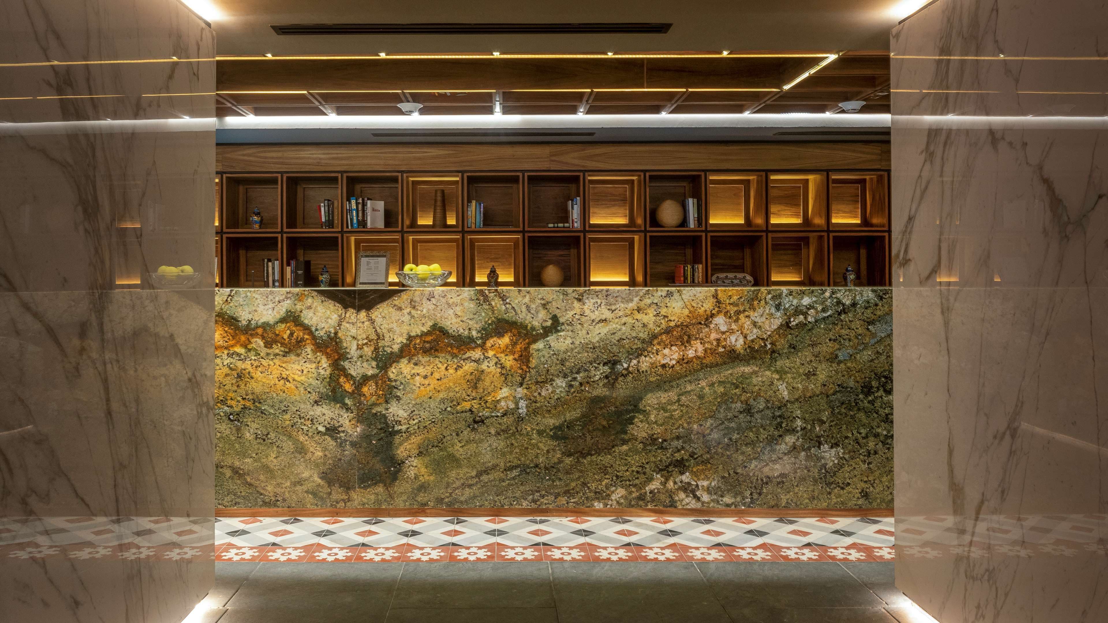 A reception area with a marble counter, wooden shelving with books, and a patterned floor.