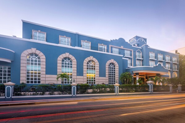 A large hotel with a blue facade, multiple arched windows, and a covered entrance area.