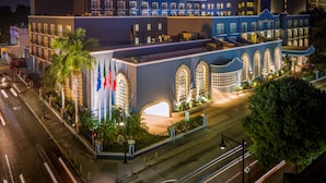 A historic building with arched windows and a central courtyard, surrounded by palm trees and flags. - Villa Mercedes Merida, Curio Collection by Hilton (Mérida)