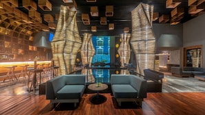 A modern lounge area with a bar, seating, and a view of a building through a glass wall. - Villa Mercedes Merida, Curio Collection by Hilton (Mérida)