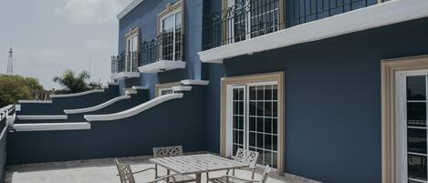 Un edificio con fachada azul, detalles blancos y un balcón con barandilla de metal.
