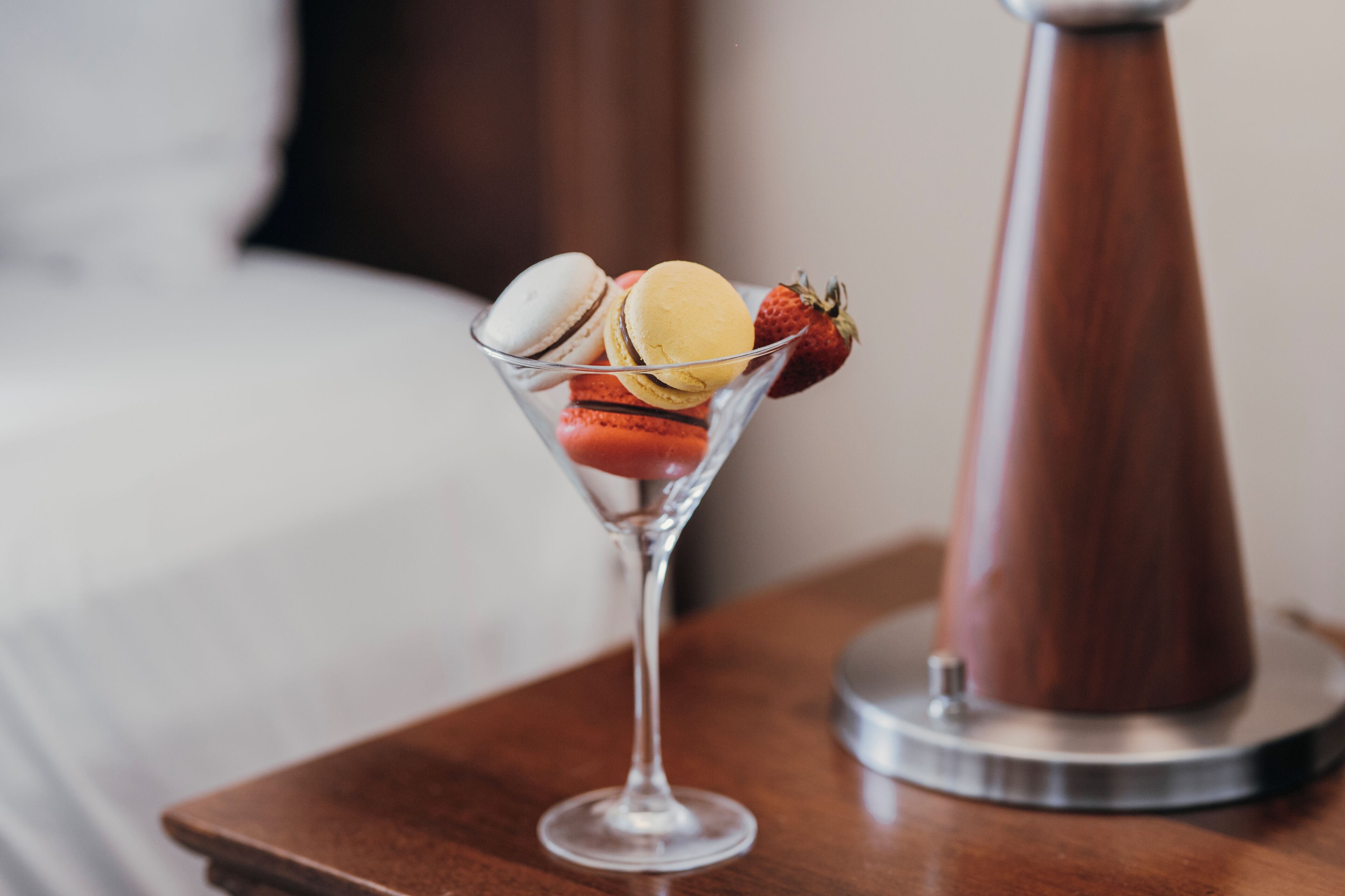 Un verre à martini, des macarons et une fraise, le tout posé sur une table en bois.