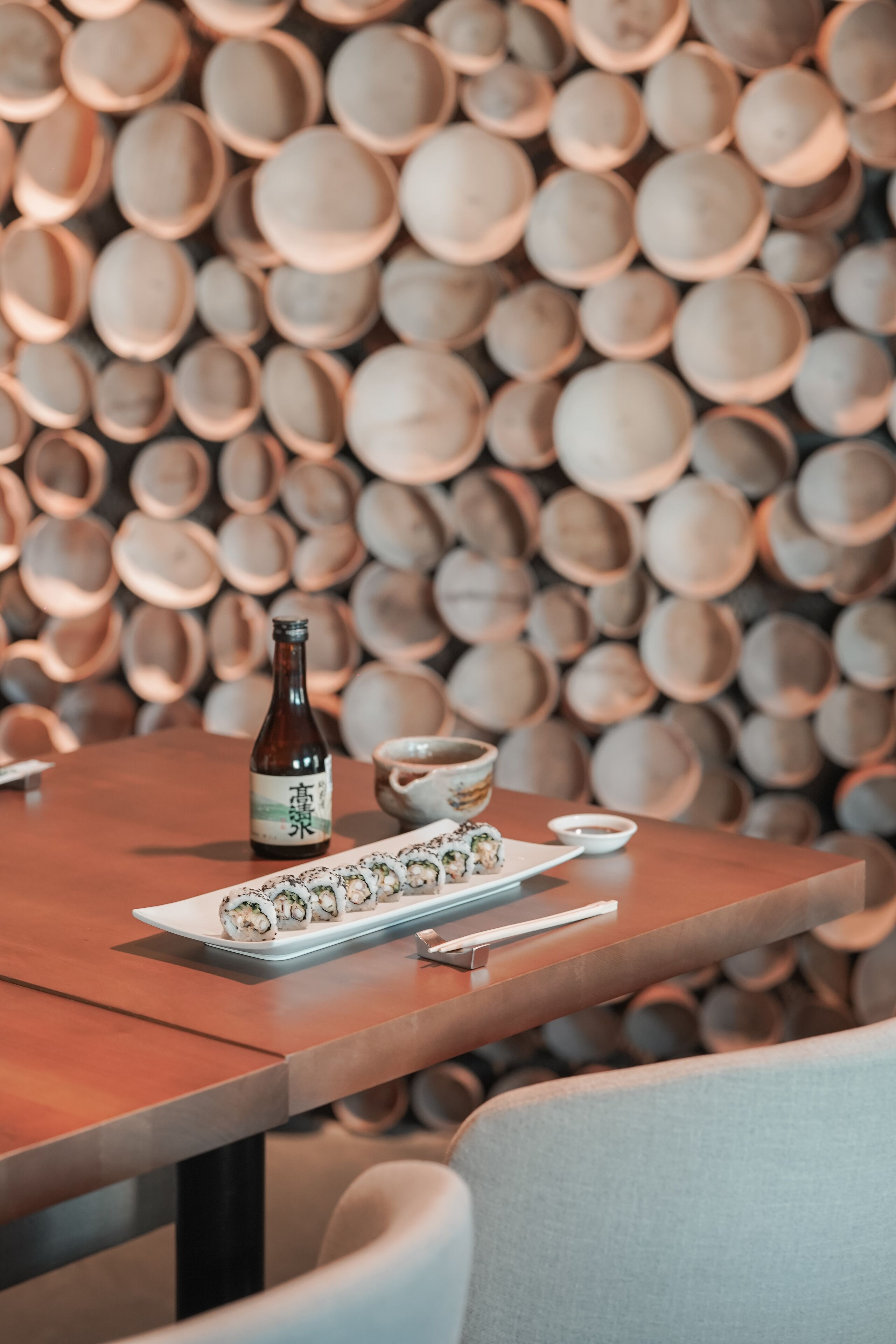 A dining table with a bottle and plates of sushi, set against a backdrop of stacked wooden bowls.