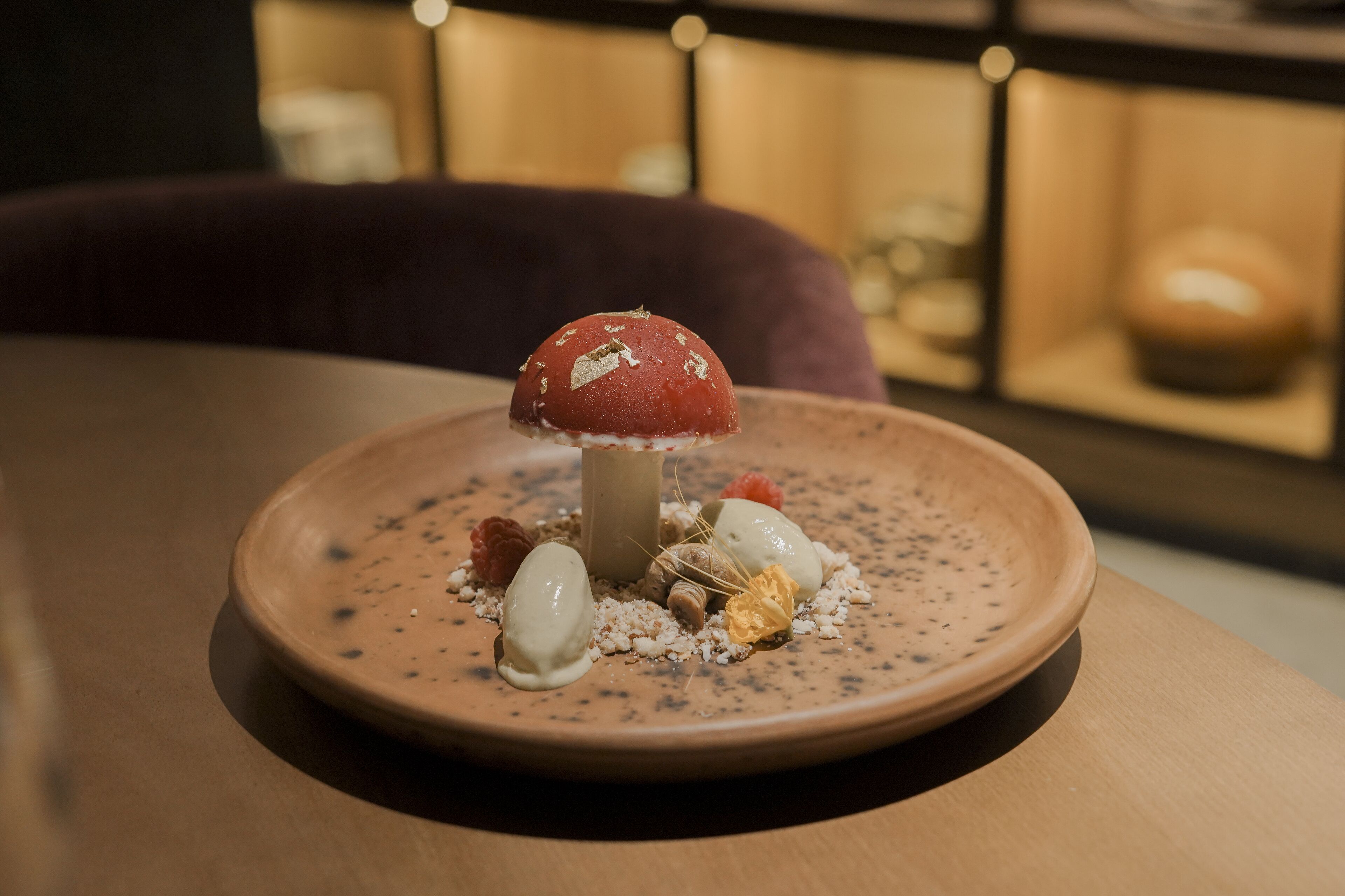 Un plato de postre con diversos elementos, incluyendo un objeto rojo con forma de hongo, un objeto esférico blanco y algunas nueces sobre un plato de cerámica con motas.