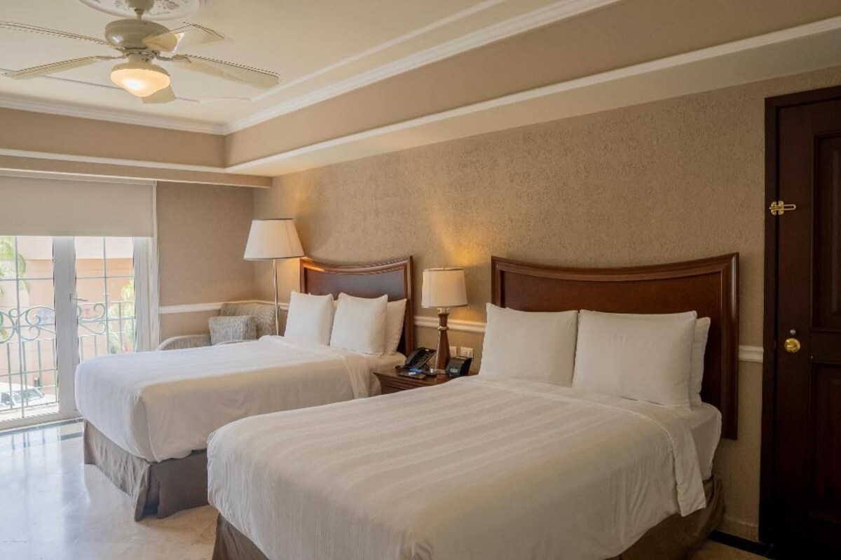 A hotel room with two beds, a ceiling fan, and a view of the outdoors.