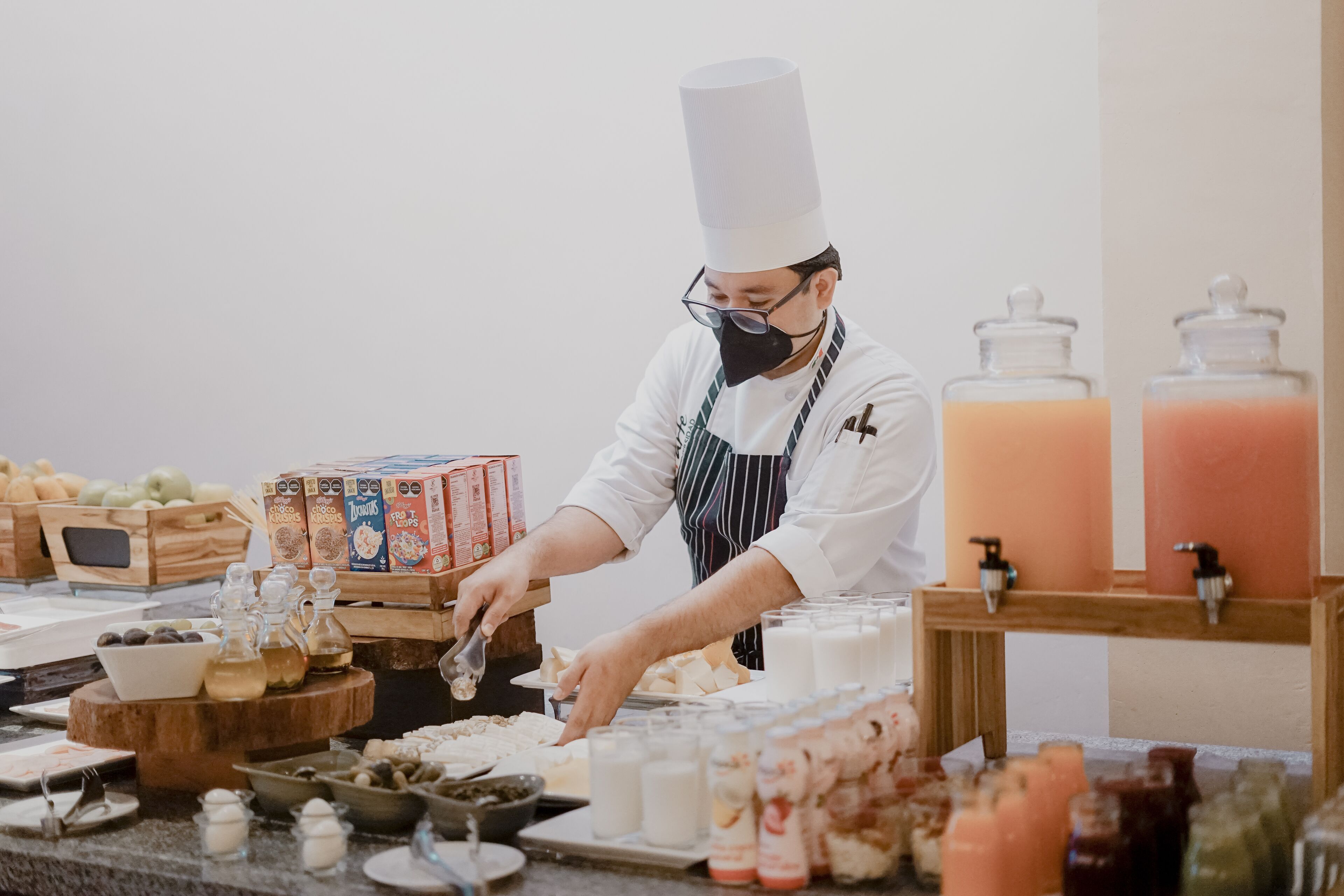 Un chef preparando comida en un bufé con varios alimentos y condimentos a la vista.