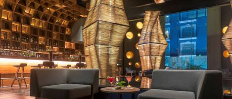 A modern bar area with a wooden ceiling, round tables, and comfortable seating.