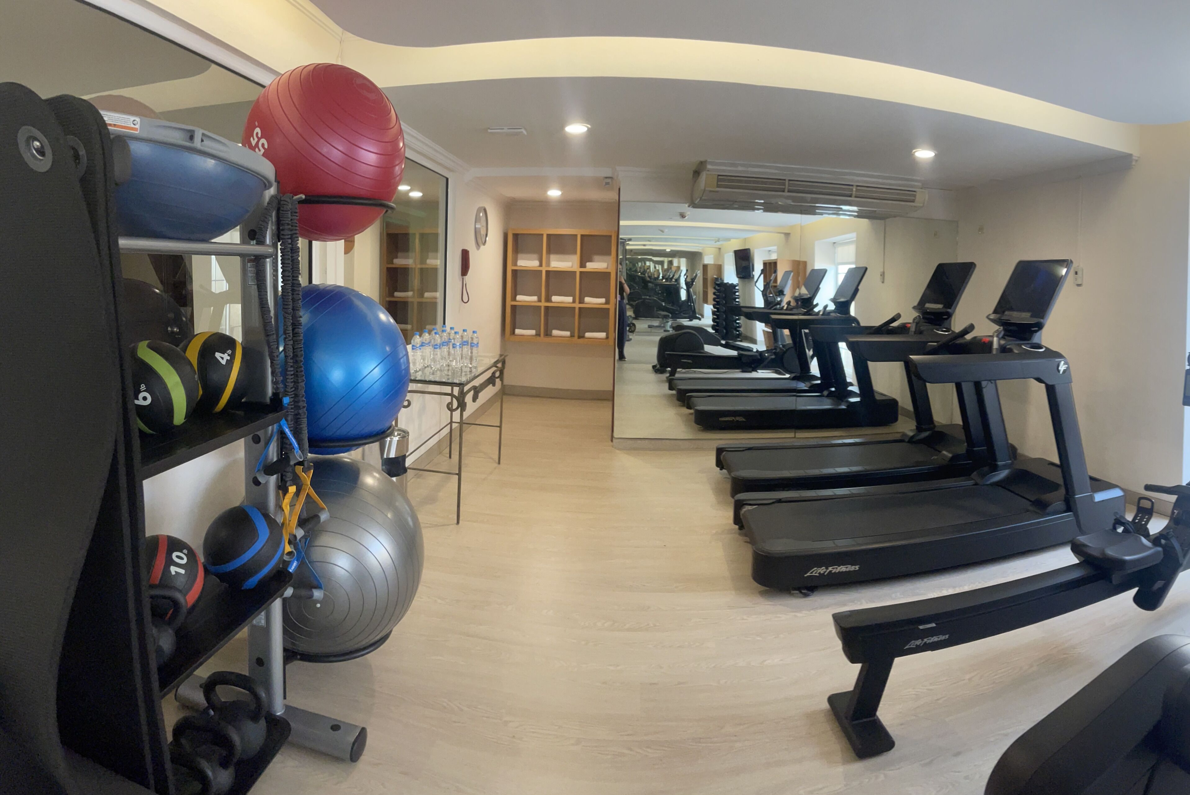 Une salle de sport équipée de tapis de course, de ballons d’exercice et de kettlebells.