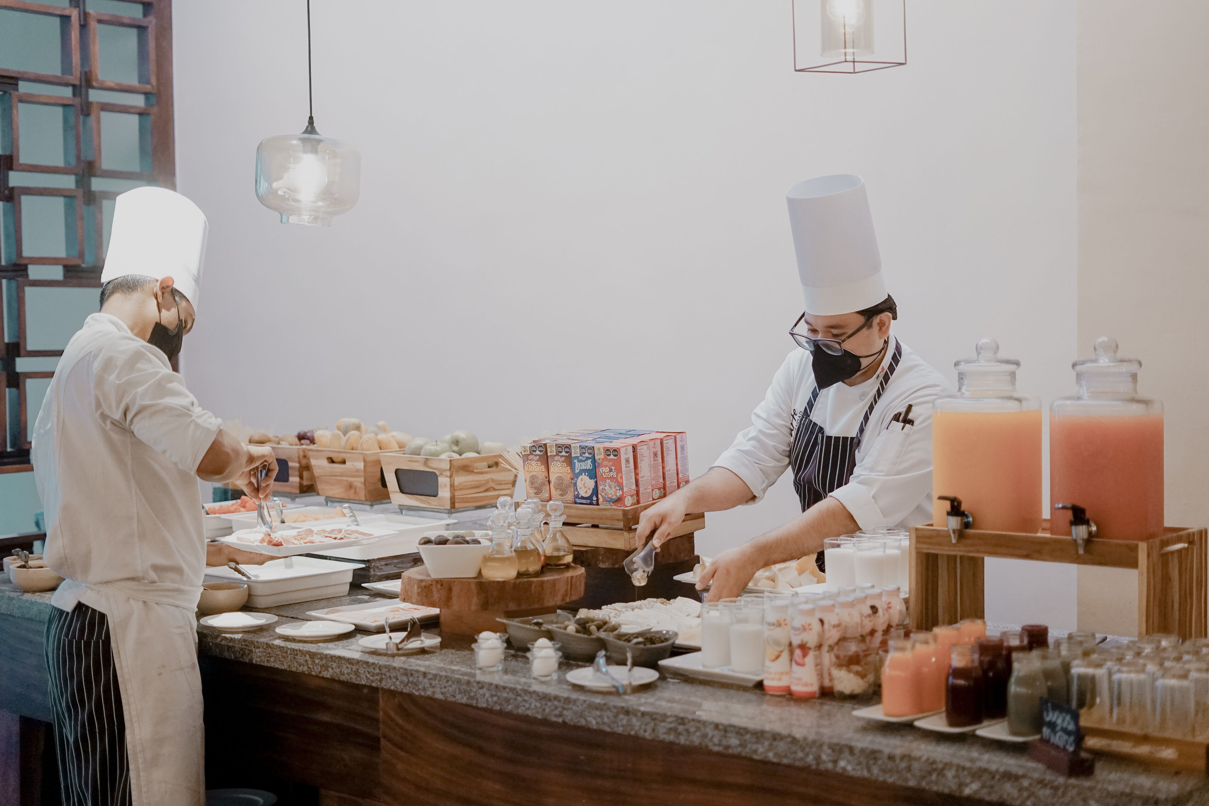 Due cuochi preparano cibo al bancone, circondati da diversi ingredienti e contenitori.