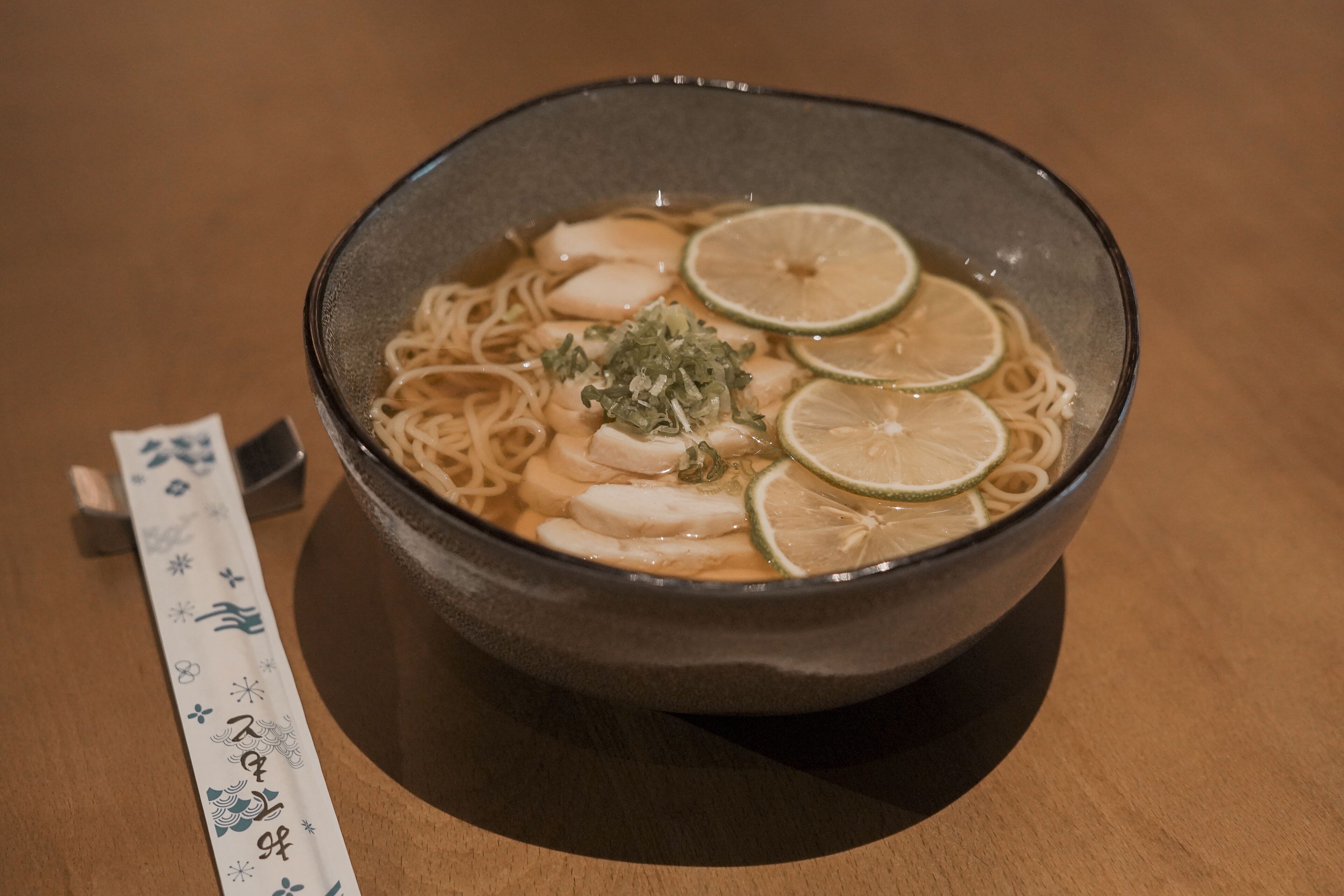 Un tazón de ramen con rodajas de lima y cebollines sobre una mesa de madera.