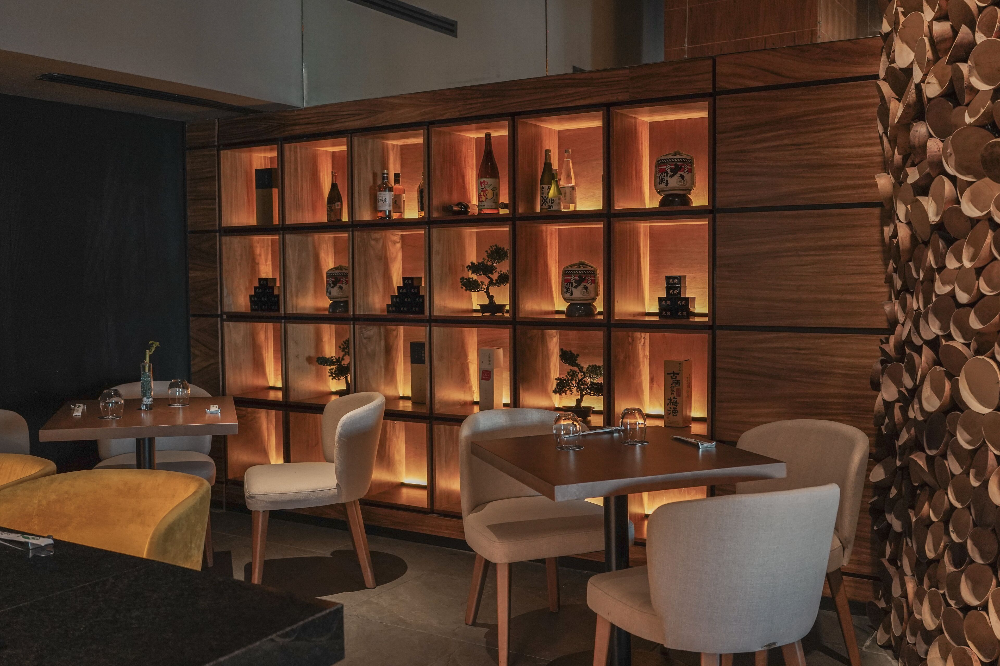 A modern dining area with a wooden wall display case containing various items. There are multiple dining tables and chairs arranged for guests.