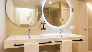 A modern bathroom with a large oval mirror, two sinks, and a towel rack.
