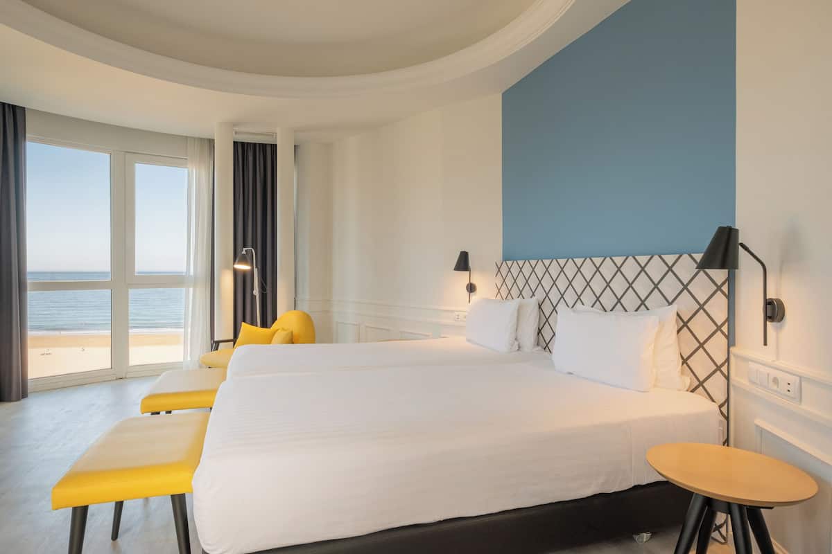 A hotel room with a large bed, a small table, and a view of the beach.