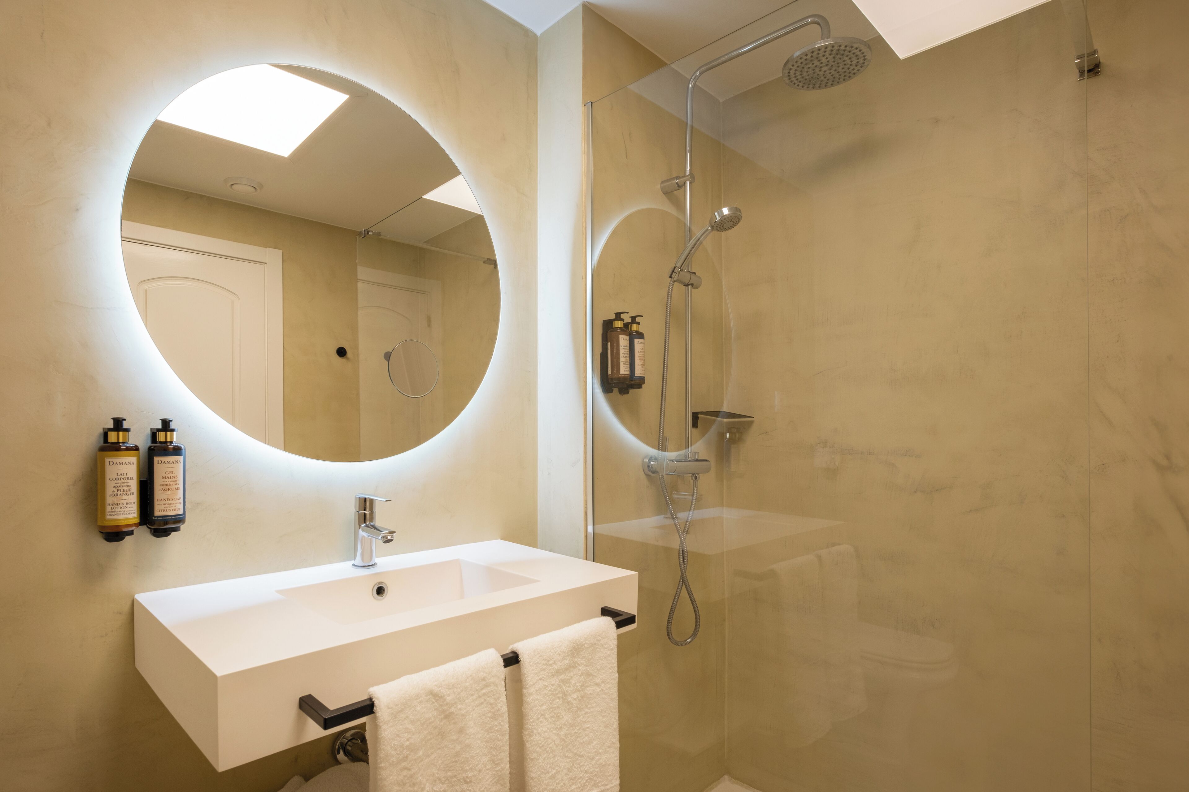 Un baño moderno con un espejo grande, un lavamanos blanco y una ducha con cerramiento de vidrio.