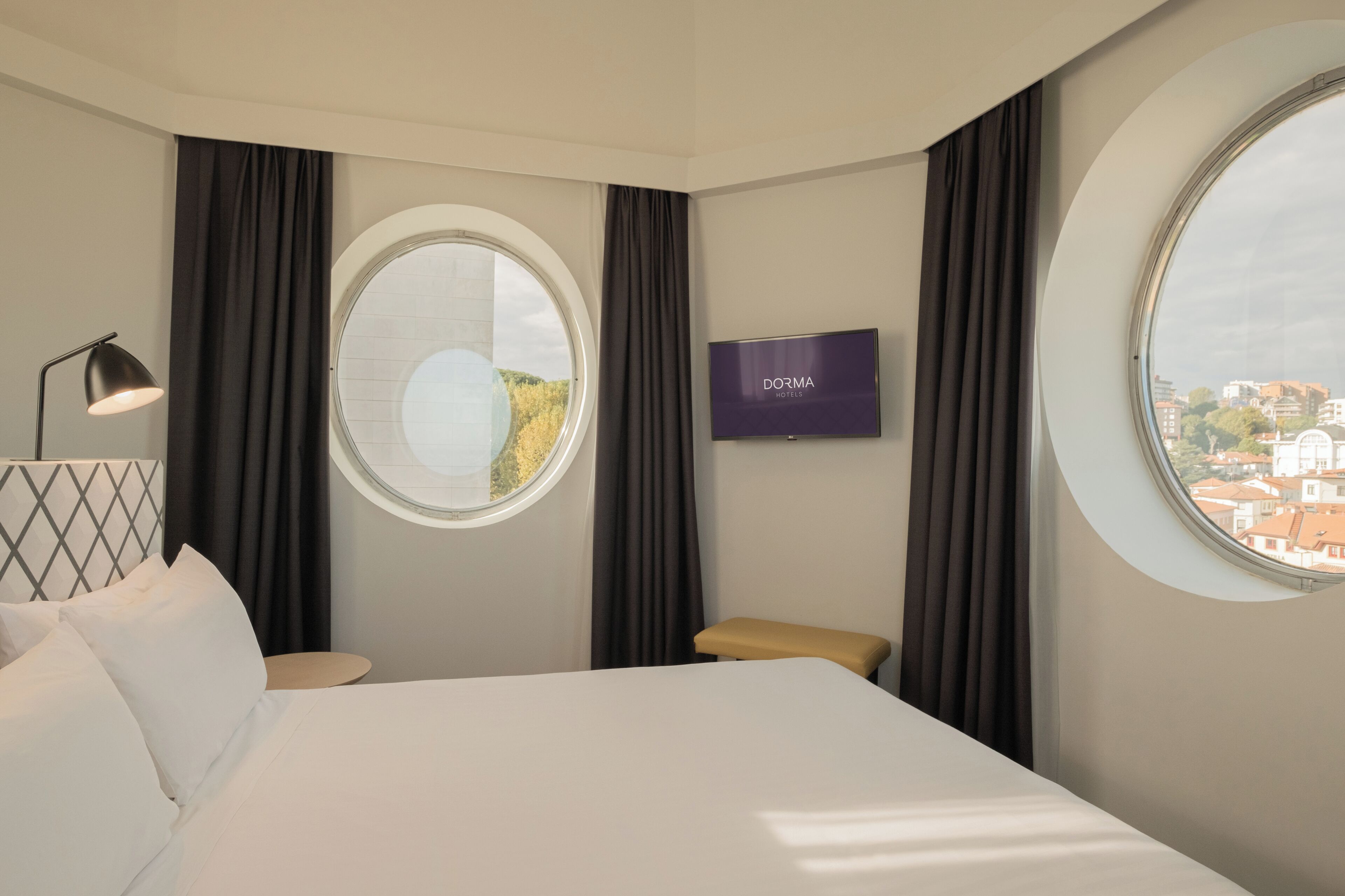 A hotel room with a bed, a TV, a window, and a view of the city.