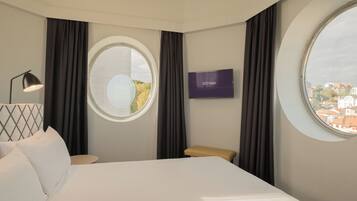 A hotel room with a bed, a TV, a window, and a view of the city.