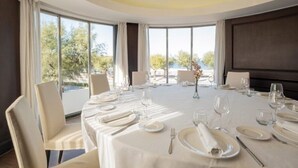 A dining room with a round table set for a meal, large windows, and a view of trees. - Dorma Sardinero (Santander)