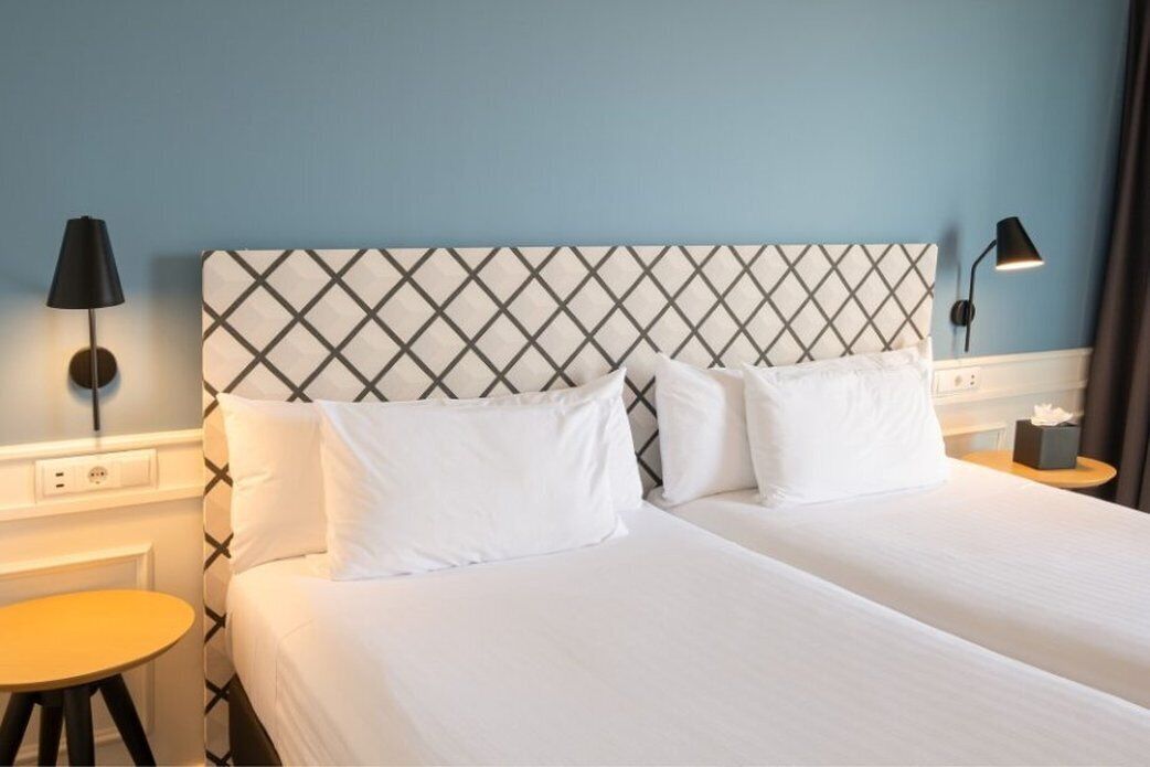 Una habitación de hotel con una cama, dos mesitas de noche y dos lámparas de pared.
