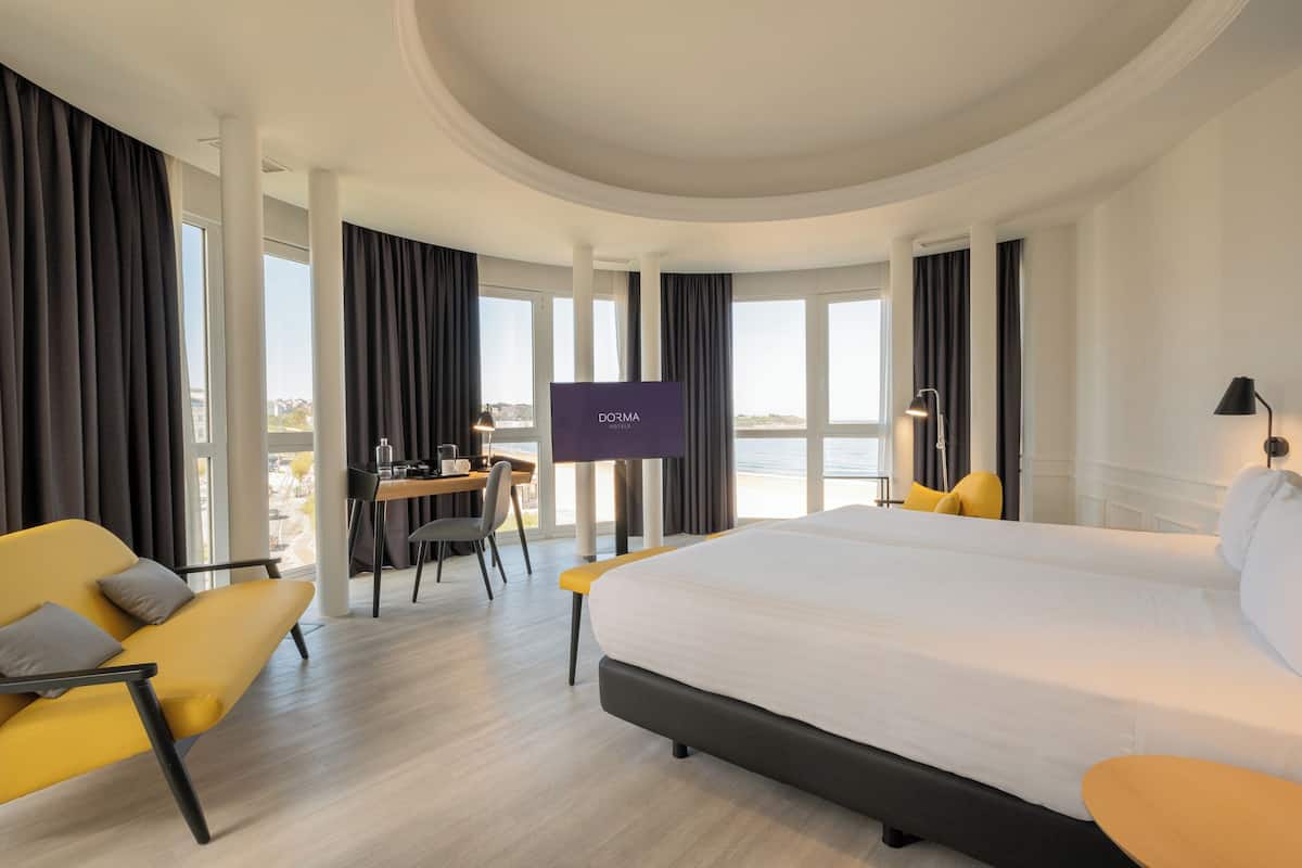 A modern hotel room with a large bed, a desk with a chair, a television, and a balcony view.