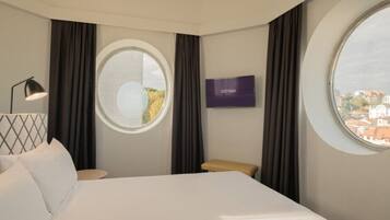 Habitación de hotel con cama, televisión, ventana redonda y vista de la ciudad.