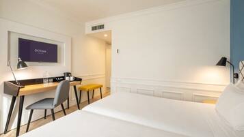 A hotel room with a bed, a desk with a chair, a television, and a lamp.