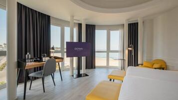 Une chambre d’hôtel équipée d’un lit, d’un bureau, d’une chaise, d’une télévision et offrant une vue sur la mer.