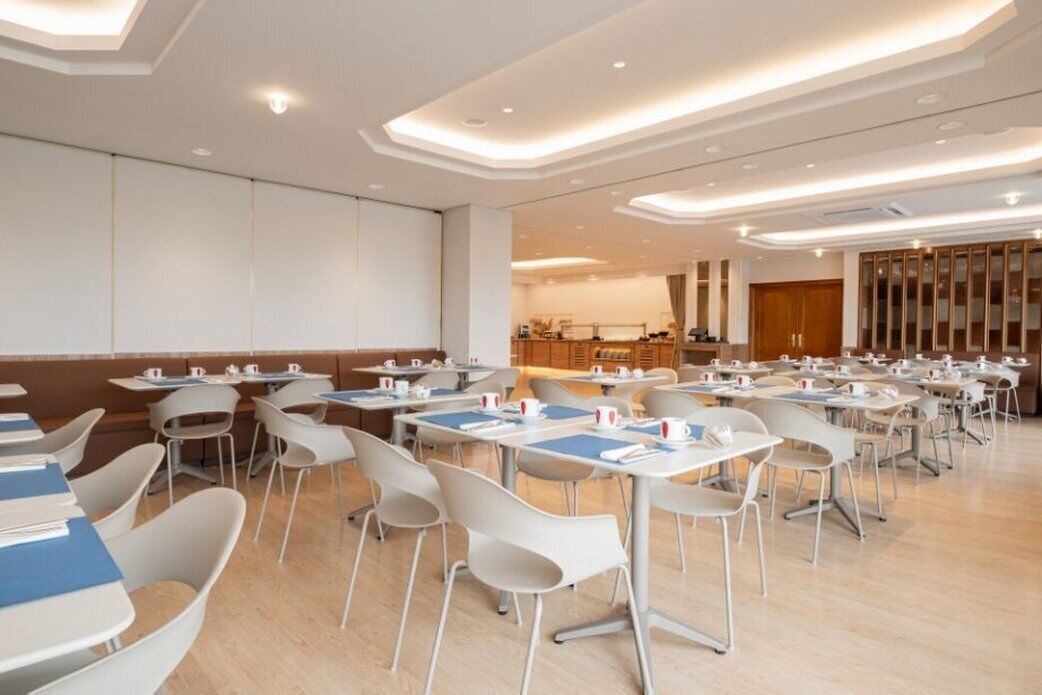 A spacious conference room with tables and chairs, a large screen, and a wooden cabinet in the background.