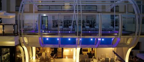 Un hotel moderno con un área de estar al aire libre con paredes de vidrio, una piscina y una entrada bien iluminada.