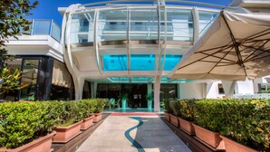 Un edificio moderno con fachada de vidrio, zona de piscina y plantas en macetas a lo largo del camino.
