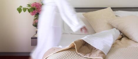 A bed with a quilted cover and pillows, a vase with pink flowers, and a red carpet.