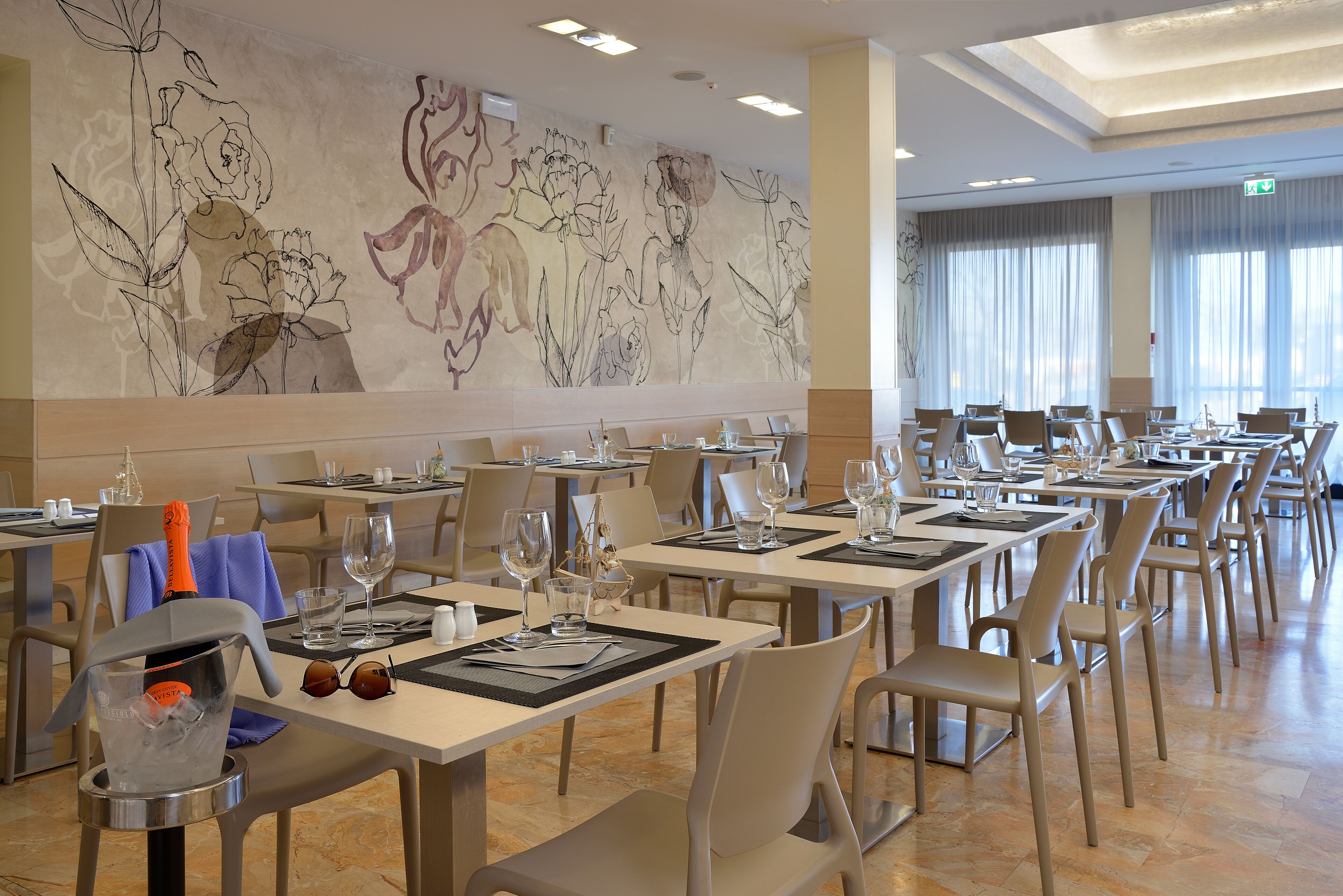 A dining area with tables set for service, a large floral mural on the wall, and a clear view of the dining area.