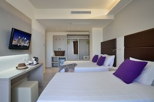 A modern hotel room with a large bed, a desk with a television, a closet, and a bathroom.