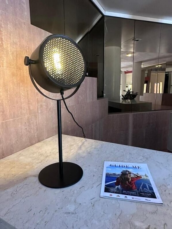 A modern room with a standing lamp, a magazine on the table, and a large mirror reflecting the room. - The St George Park Hotel (St. Julian's)