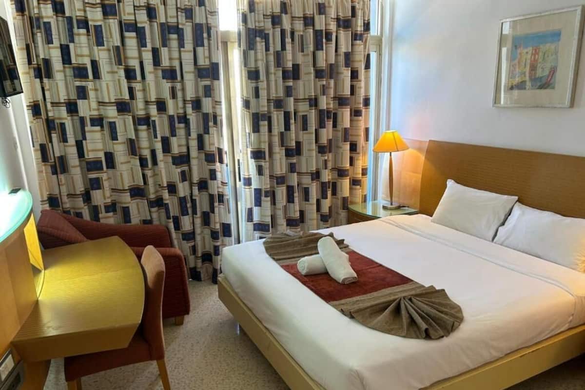 Una habitación de hotel con cama, escritorio, silla, lámpara y cortina estampada.