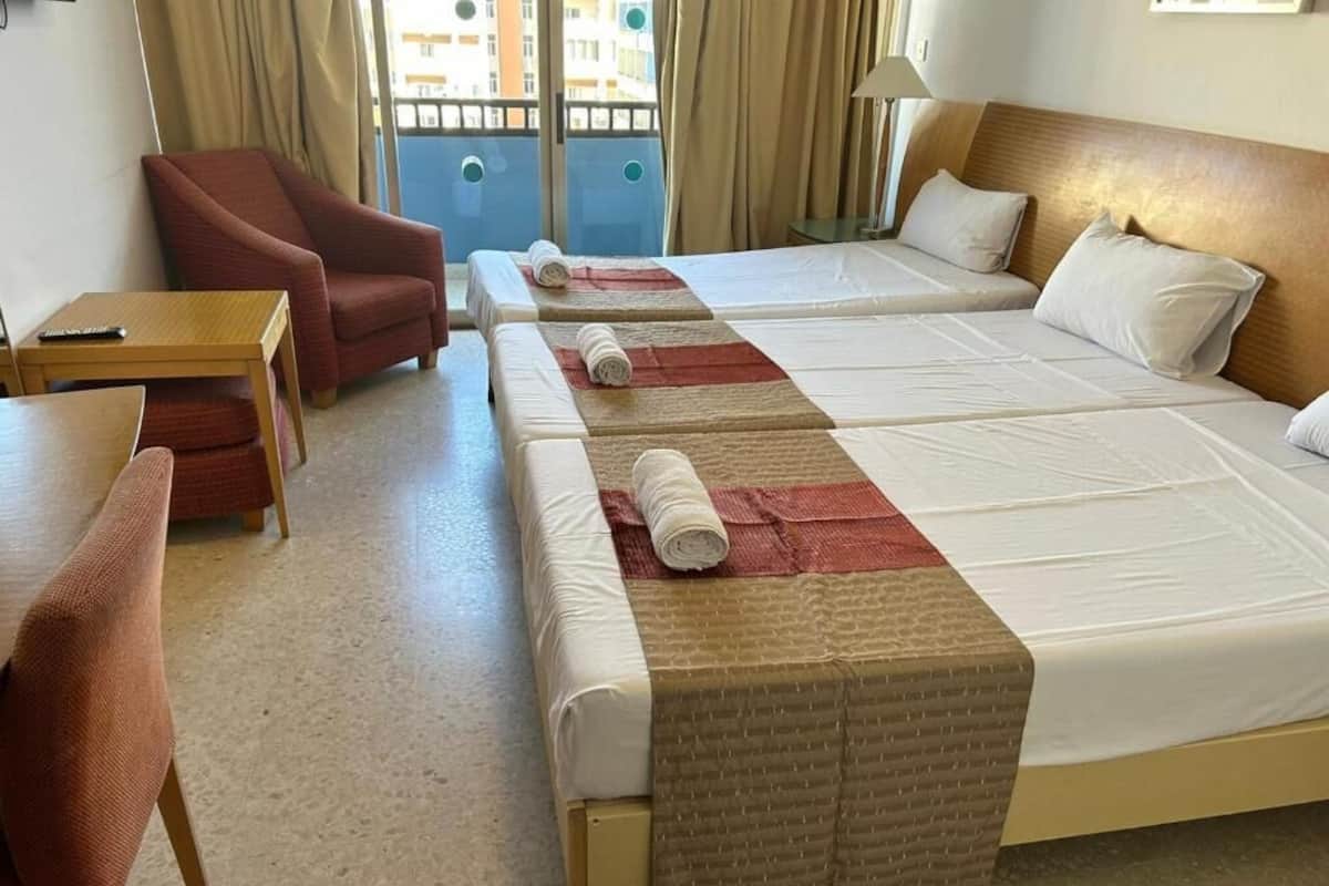 Habitación de hotel con dos camas, una silla, una mesita y vista al exterior.