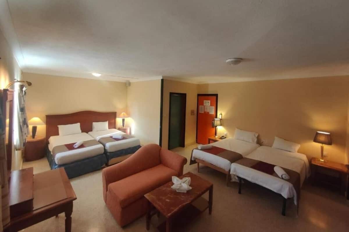 Habitación de hotel con dos camas individuales, un sofá, una mesita y un escritorio.