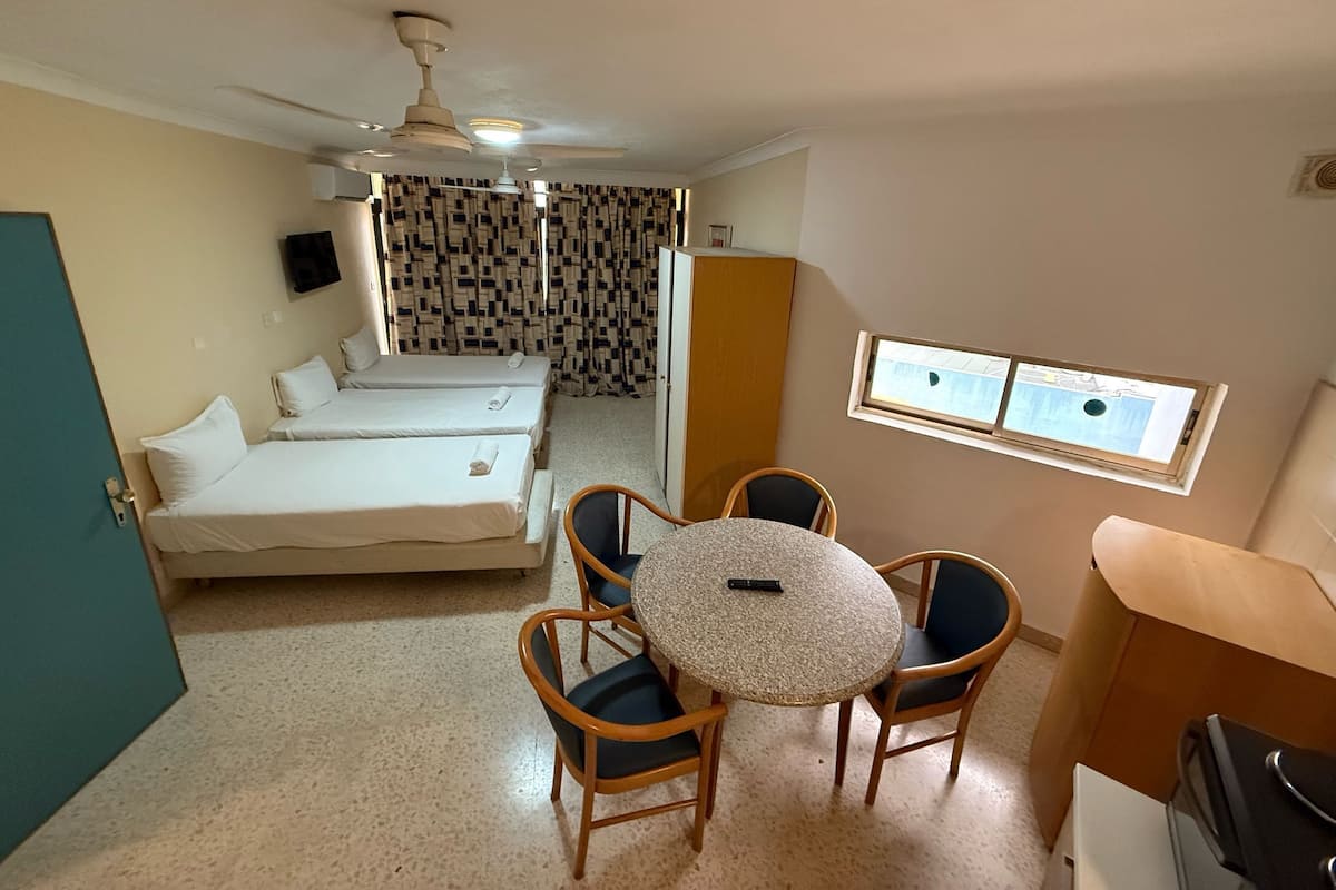 Una habitación con dos camas, una mesa de comedor con sillas, un ventilador de techo, una ventana con vistas y una puerta.