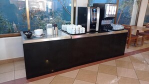 Una zona de recepción con una máquina de café, tazas y un bol de fruta.