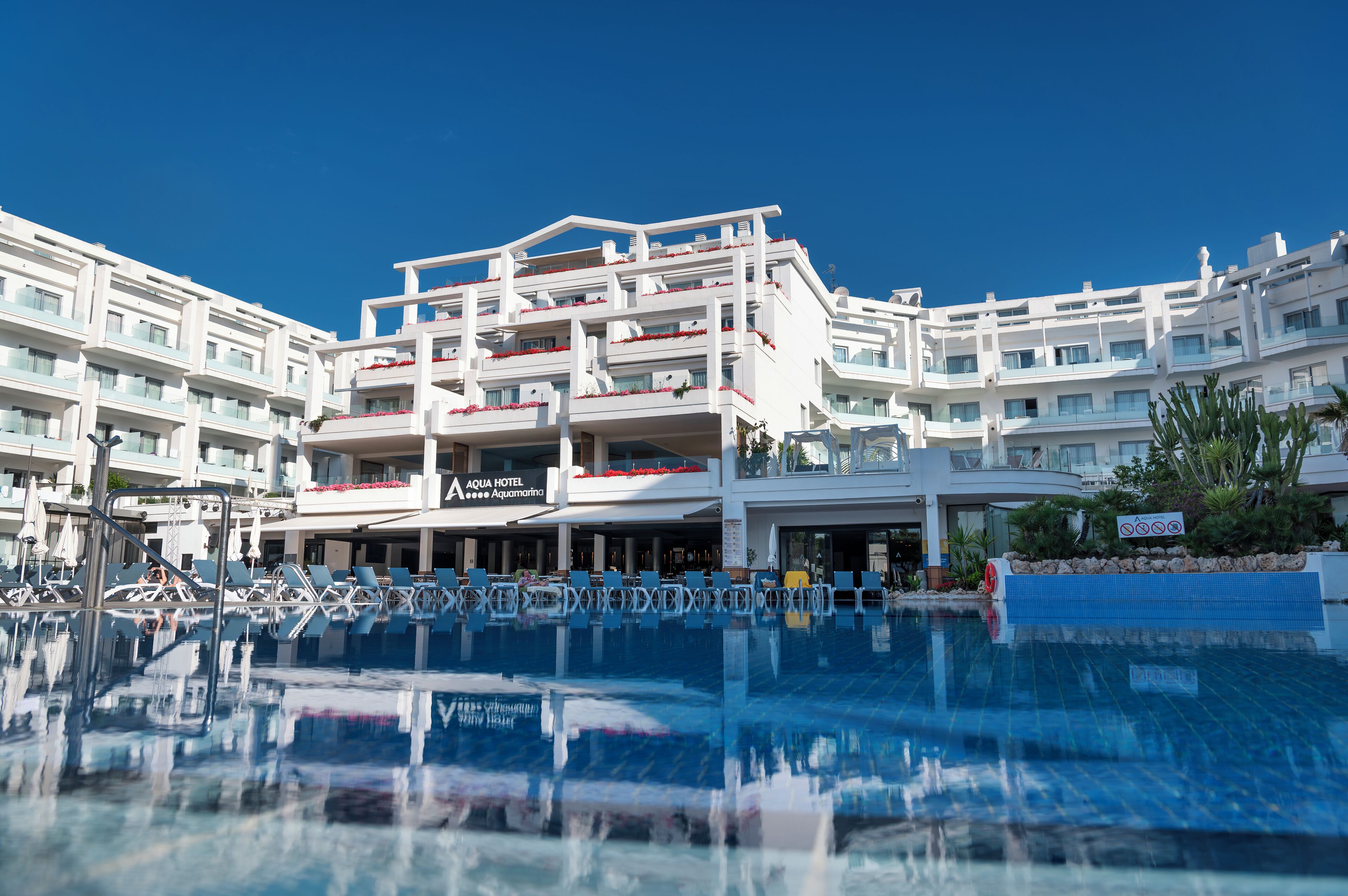 Een hotel met meerdere balkons, een zwembad en een helderblauwe lucht.
